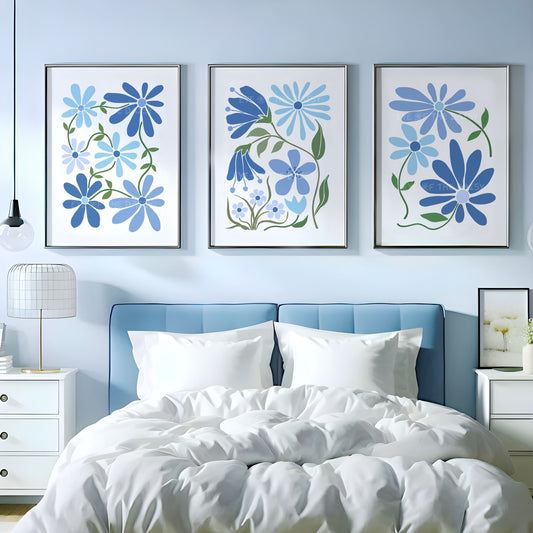 Set of three abstract botanical wall art prints of stylized flowers in different shades of blue on a white background above a bed in a blue bedroom