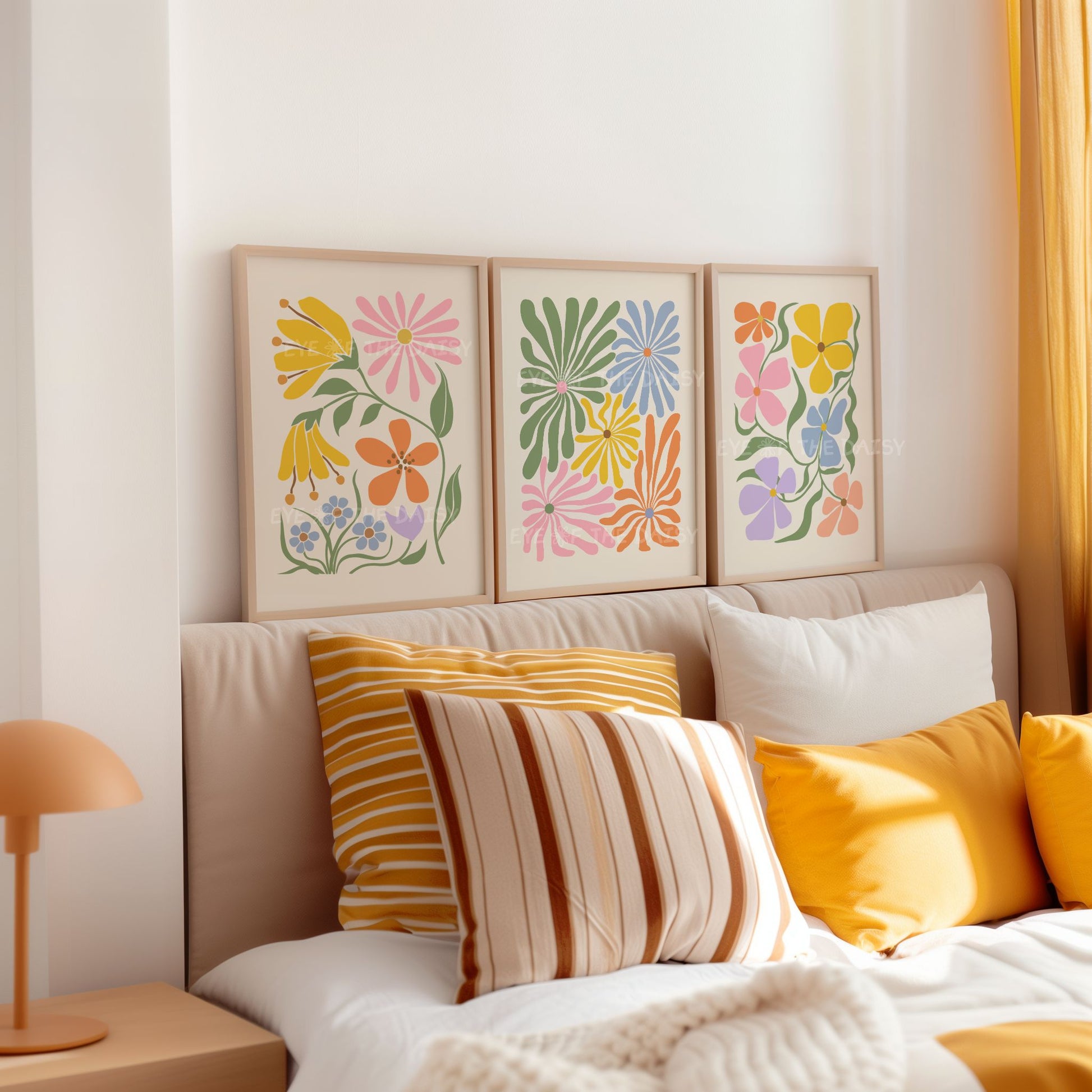 A set of three vibrant botanical abstract digital prints above a bed in a bedroom with colorful retro abstract flower cut-outs