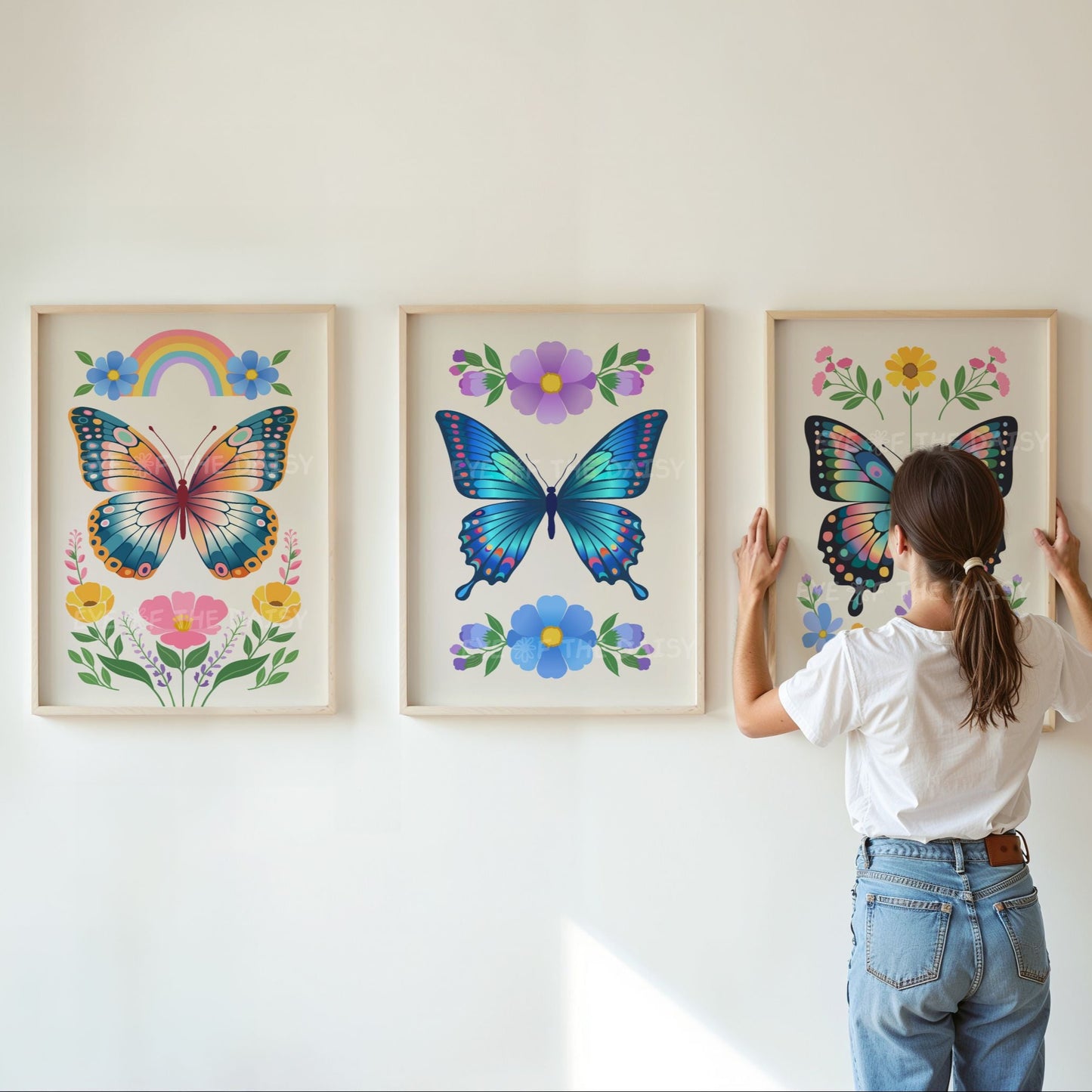 Person hanging three framed prints of vibrant boho colourful floral butterfly artworks on a wall that are in a boho folk art style