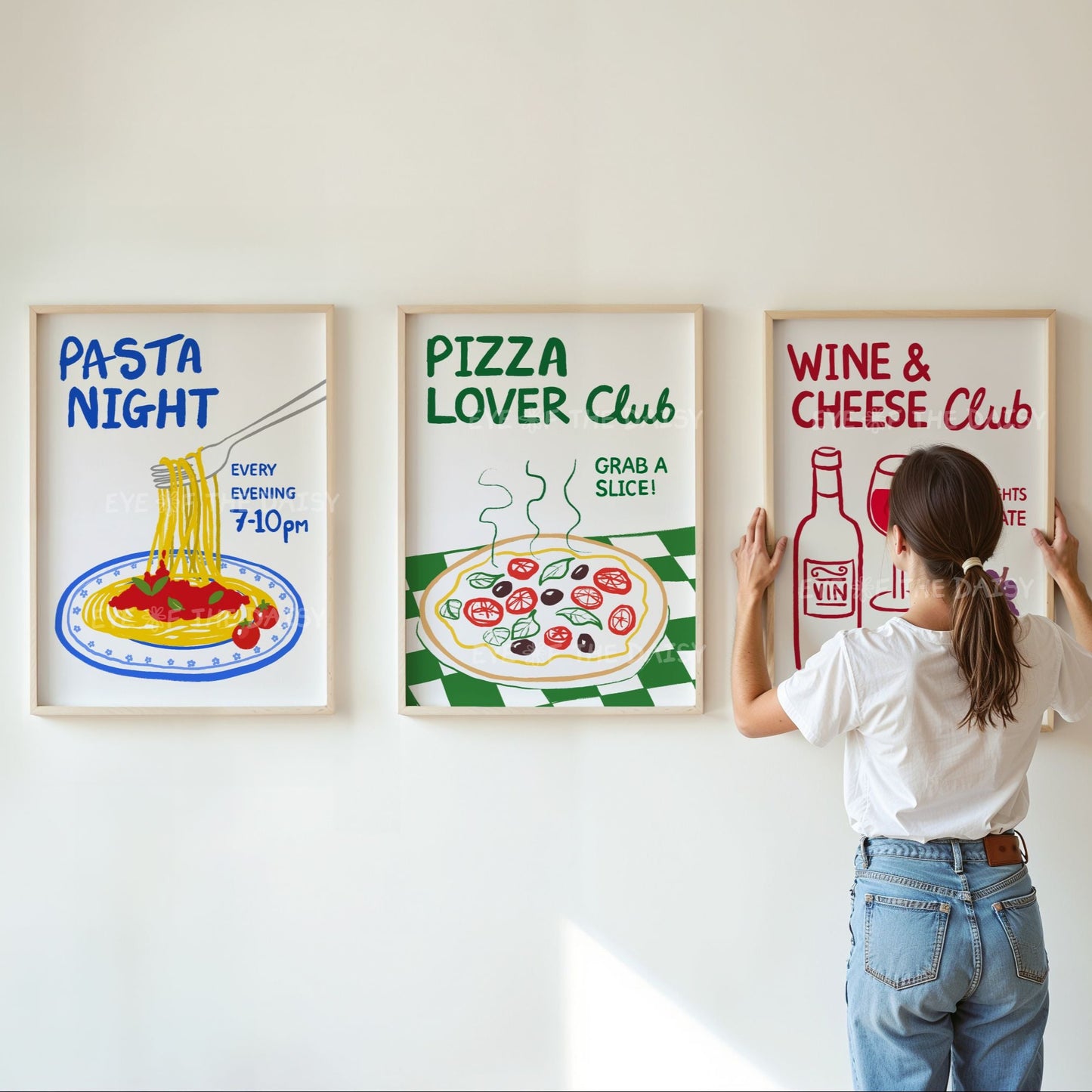 Woman hanging framed prints on a wall with funny 'Pasta Night', 'Pizza Lover Club', and 'Wine & Cheese Club' trendy artwork